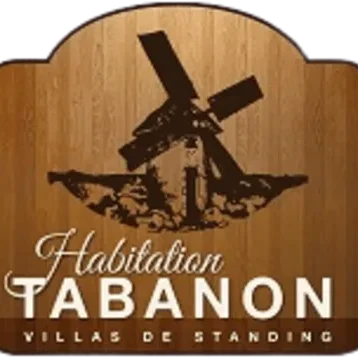 L'image présente le logo de Habitation Tabanon, avec un visuel évoquant un moulin à vent stylisé, ancré dans un cadre en bois, ce qui rappelle un côté rustique et traditionnel. Le texte "Habitation Tabanon" est écrit en lettres blanches élégantes, avec la mention "Villas de standing" juste en dessous, indiquant que cette entreprise est spécialisée dans des logements haut de gamme.